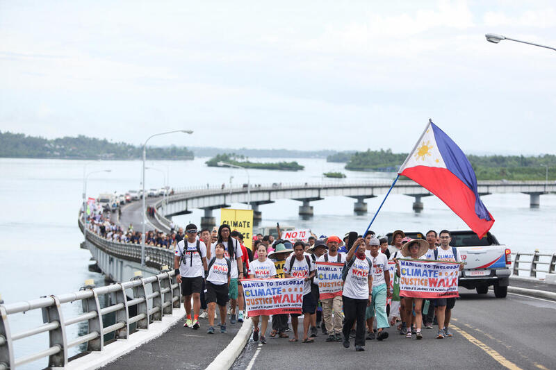 A big group of climate justice walkers are crossing a bridge carrying the Philippines' flag