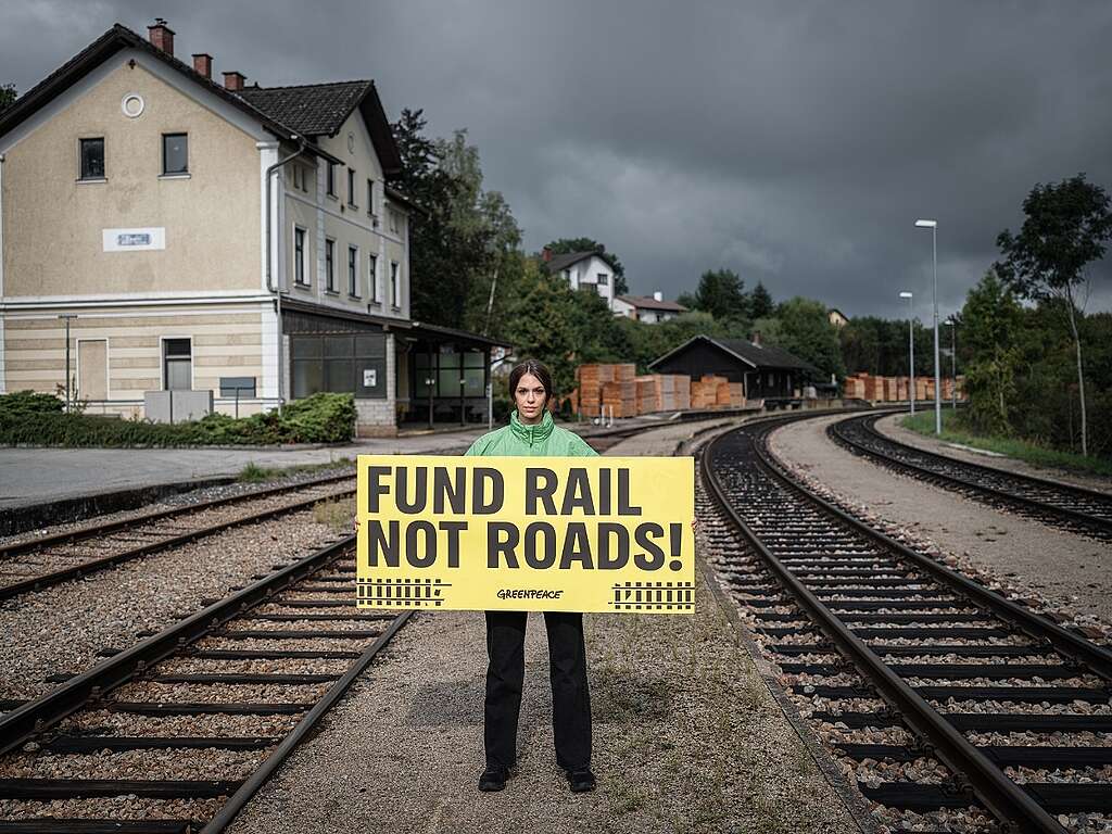 Greenpeace Austria hols a banner saying "Fund rail not road" in a closed train station.