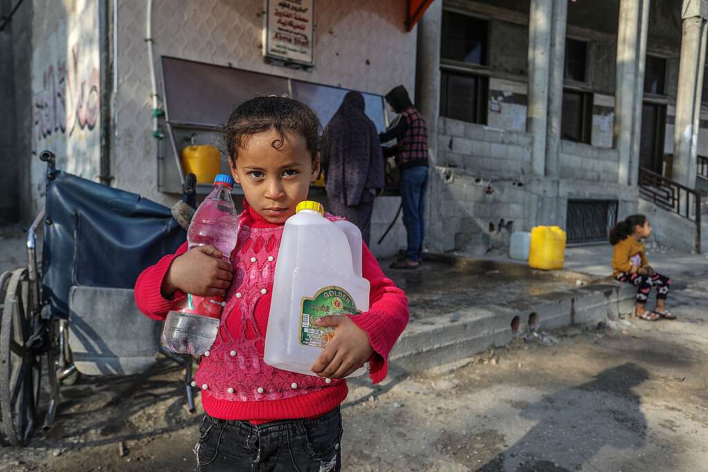 A young palestinian girl holds bottles of water near a water refilling station. Palestinians fill bottles of water for home consumption from a public fountain, at the Rafah refugee camp in the southern Gaza Strip. © Anas Mohammed / Shutterstock