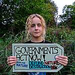 Activist with banner that reads, "Governments act now! Defund Nature Destruction Now. #HopeForNature" 