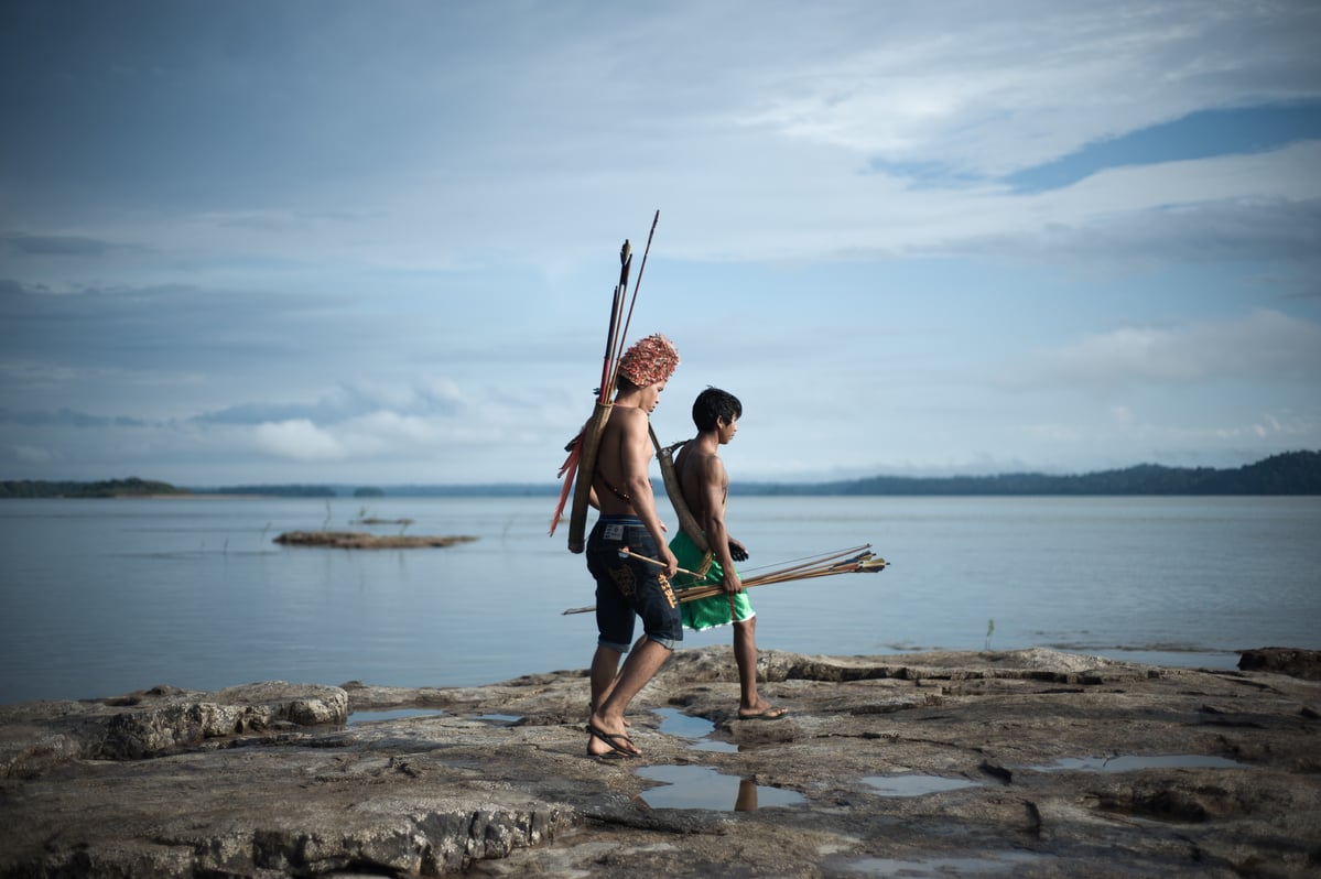 Two Munduruku men walk along a river, holding spears © Anderson Barbosa / Greenpeace