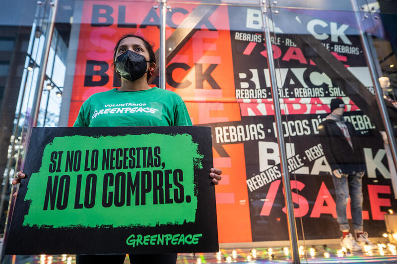 Activista de Greenpeace sosteniendo un cartel que dice “Si no lo necesitas, no lo compres.” frente a una tienda de descuentos