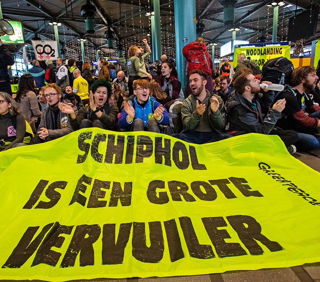 Schiphol moet krimpen. Geel spandoek op Schiphol met de tekst: 'Schiphol is een grote vervuiler'.