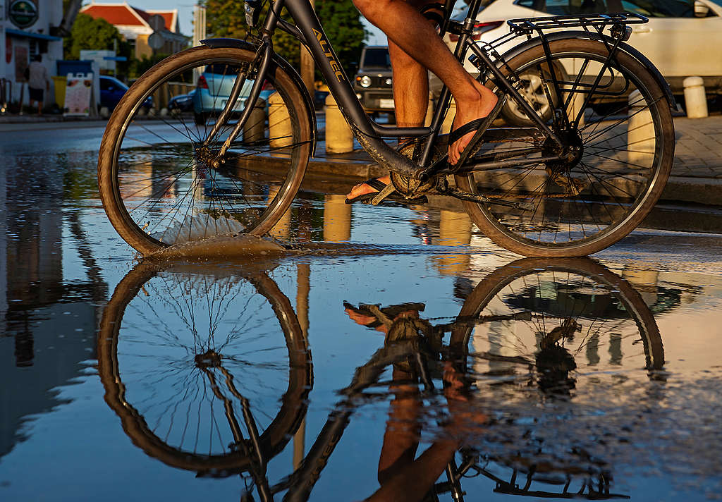 Een fietser rijdt door regenplassen op Bonaire, waar twee van de vijf mensen in armoede leven. De Consumentenbond start een rechtszaak. 