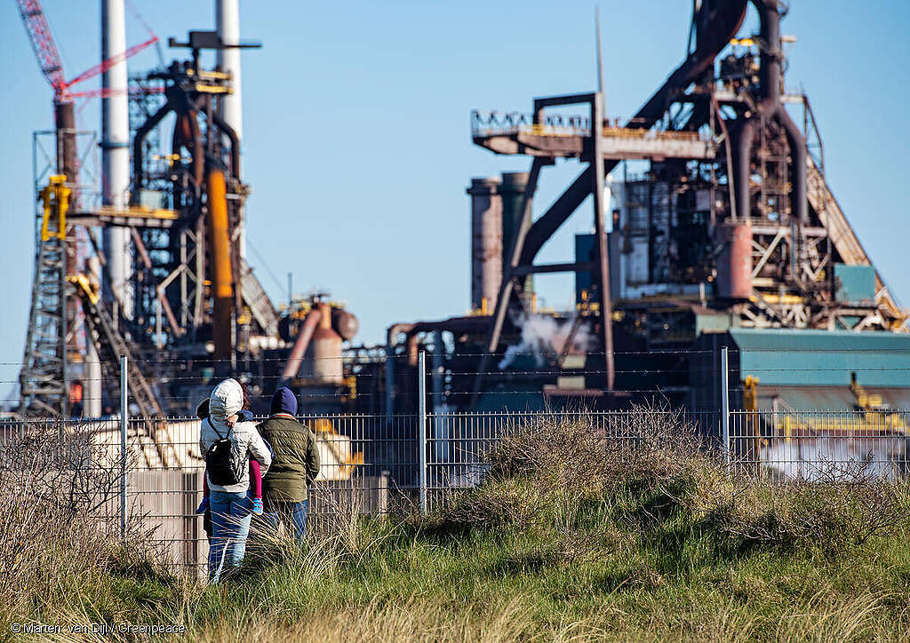 Mensen kijken door het hek van het terrein van de staalfabriek van Tata Steel.