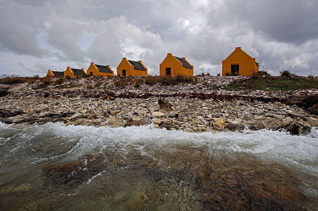 Zicht op de oranje (oorspronkelijk okergeel) slavenhutjes langs de zuidwestkust van Bonaire, waarop goed te zien is hoe dicht bij zee ze liggen. De hutjes dienden in de negentiende eeuw als onderkomen voor de tot slaaf gemaakten die tewerkgesteld werden in de zoutpannen. De slavenhutjes van Bonaire zijn uniek, omdat op veel andere plekken met een slavernijverleden herinneringen daaraan zijn verwijderd. Bonaire is een eiland in het Caribische deel van Nederland, dat bestuurlijk een bijzondere gemeente van Nederland vormt. Het is gelegen in het zuidelijke deel van de Caribische Zee, voor de kust van Venezuela, en behoort tot de ABC-eilanden van de Kleine Antillen.