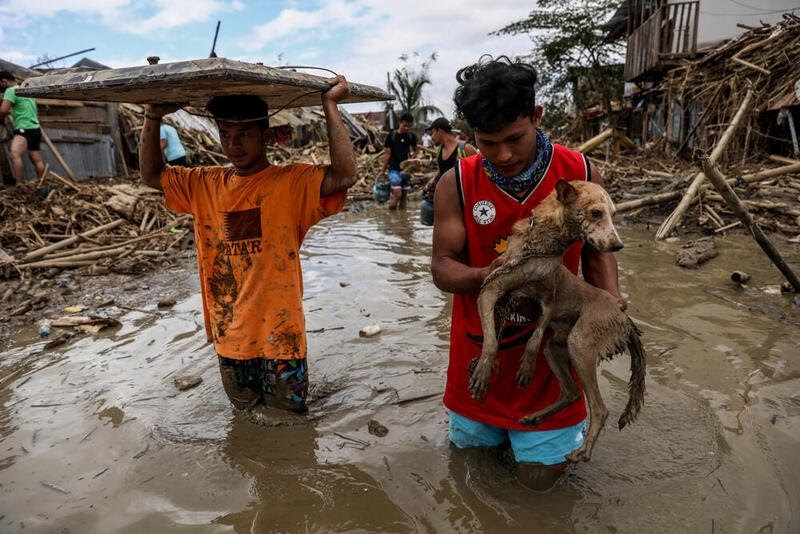 En mann bærer hunden sin gjennom en oversvømt gate, full av gjørme etter tyfonen Ulysses – byen Rodriguez i Rizal-provinsen øst for Manila.