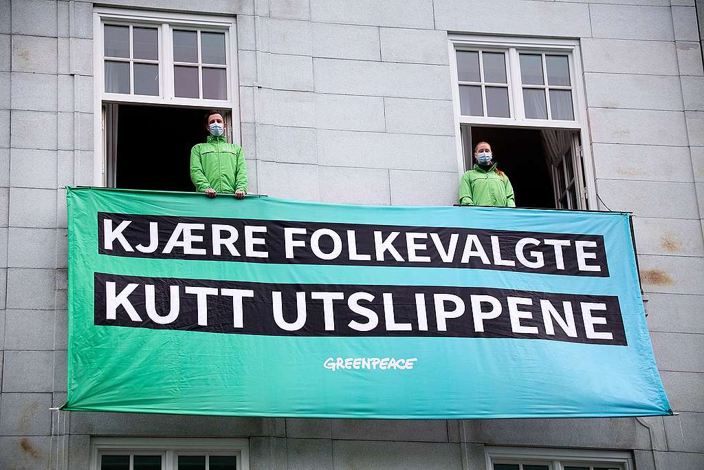 To Greenpeace-aktivister står i hvert sitt vindu på Grand Hotel i Oslo med et banner med teksten "Kjære folkevalgte, kutt utslippene"