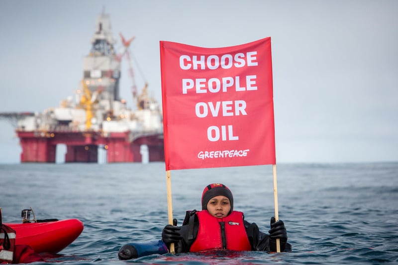 Greenpeace-aktivist i vannet holder et banner med teksten "Choose people over oil" - "Velg mennesker framfor olje". Statoil-oljeriggen Songa Enabler i bakgrunnen.