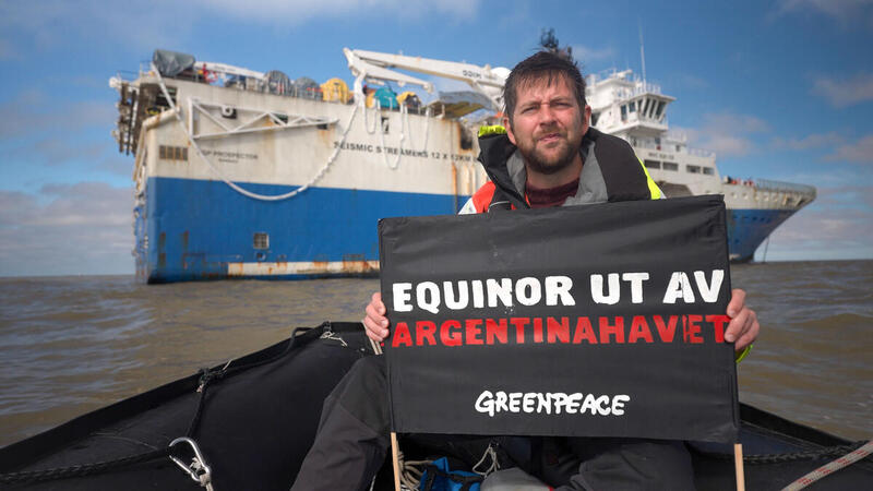 Aktivist Halvard Raavand holder et banner med beskjeden "Equinor ut av Argentinahavet" foran skipet som Equinor har hyret for å utføre seismikkskyting.