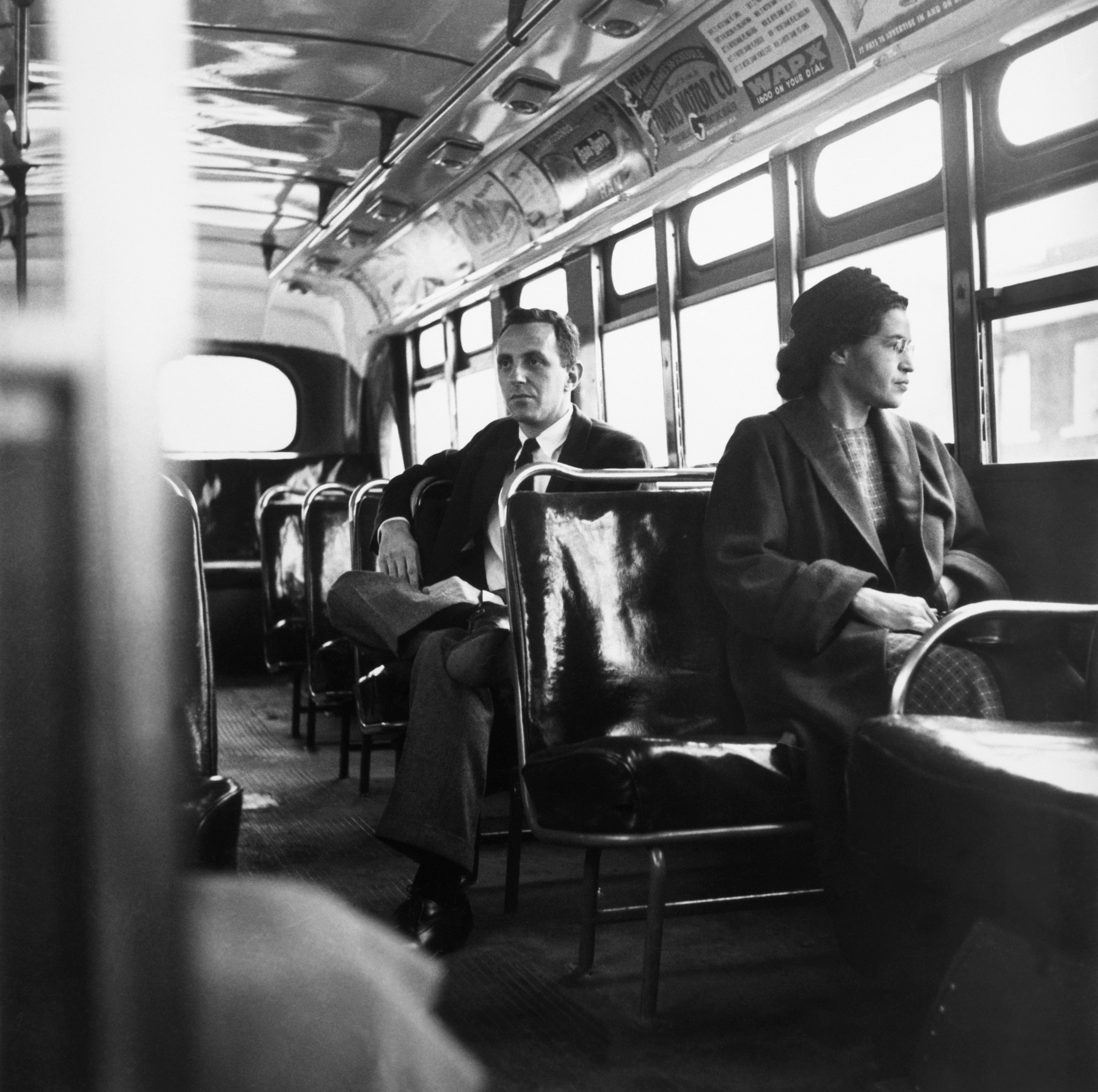 B&W Photo of Rosa Parks sits in the front of a bus in Montgomery, Alabama, after the Supreme Court ruled segregation illegal on the city bus system on December 21st, 1956. Parks was arrested on December 1, 1955 for refusing to give up her seat in the front of a bus in Montgomery set off a successful boycott of the city busses. Man sitting behind Parks is Nicholas C. Chriss, a reporter for United Press International out of Atlanta.