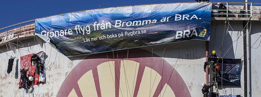 Flygbolaget BRAs reklamaffisch för sitt “gröna” inrikesflyg sätts upp av aktivister på Shells raffinaderi i Rotterdam.