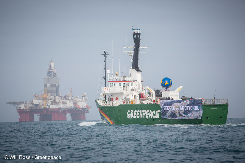 Greenpeace-fartyget MY Arctic Sunrise vid en oljerigg med en stor flagga med texten "Människor eller olja i Arktis"