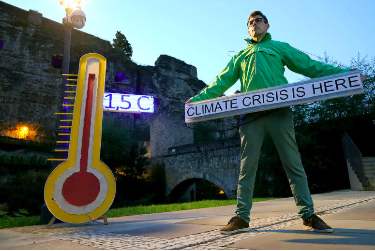 Aktivist med stor termometer och skylt där det står klimatkrisen är här