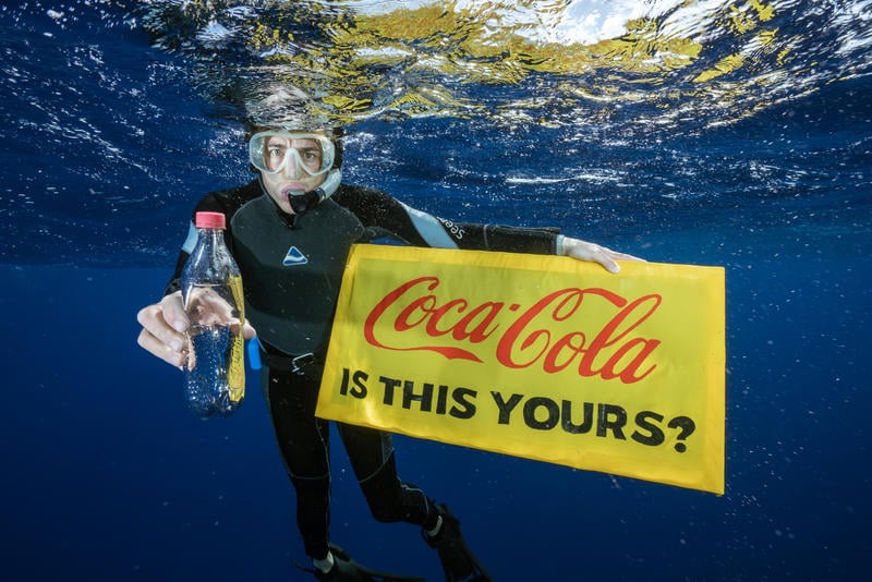 Dykare från Greenpeace håller upp en plastflaska som hittats i Stilla havet och visar en skylt med texten: Coca-cola is this yours? 