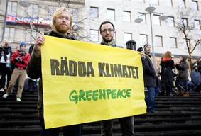 Demonstration, två personer håller upp en gul banderoll som det står "Rädda klimatet" på