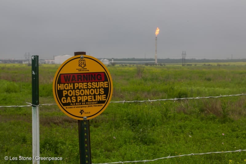A sign on a fence line near Westhoff warning about the danger of a high pressure gas pipeline at the site. Gas is burned off at the flare in the background at an Eagle Ford shale fracking installation in DeWitt County.
