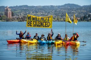 8 kayaking activists hold "we will not be silenced" signs in a row